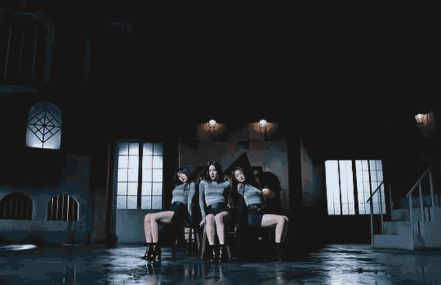 three women sitting on stools in a dark room with windows