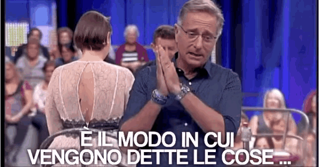 a man and a woman are sitting in front of a crowd and the man is making a gesture with his hands .