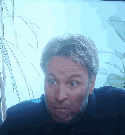 a man with gray hair and a beard is looking at the camera with a surprised look on his face