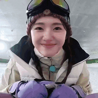 a woman wearing a hat , goggles , and gloves is smiling while holding a snowboard .
