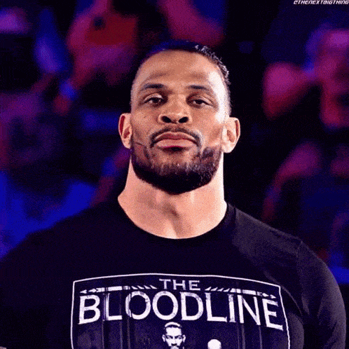 a man with a beard wearing a black t-shirt that says the bloodline is giving a peace sign .