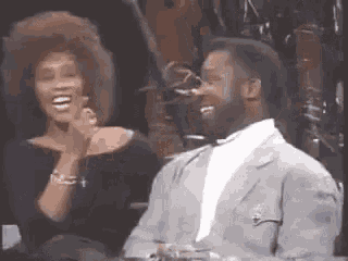 a man and a woman are laughing together while sitting at a table in front of a microphone .