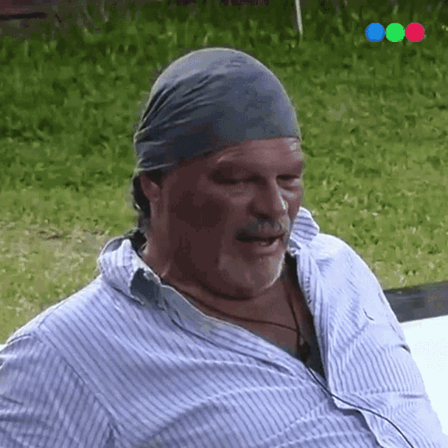 a man wearing a bandana and a striped shirt is sitting outside