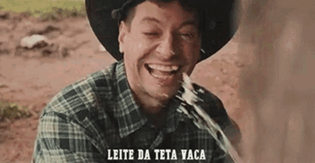 a man in a cowboy hat is drinking milk from a cow 's udder .
