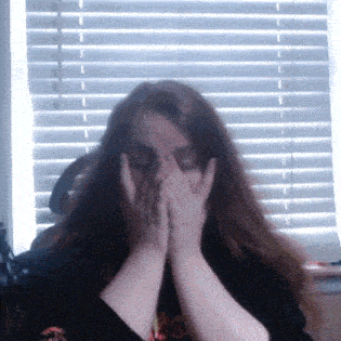 a woman is covering her face with her hands while sitting in front of a window .
