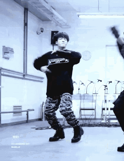 a man in a black shirt and camo pants is dancing in a room with a clock on the wall .