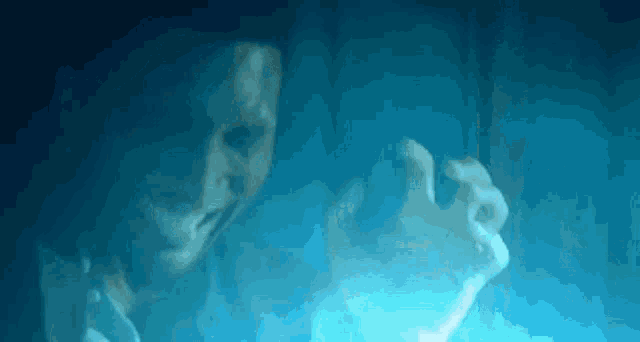 a close up of a person 's face and hands in a dark room with a blue light behind them .