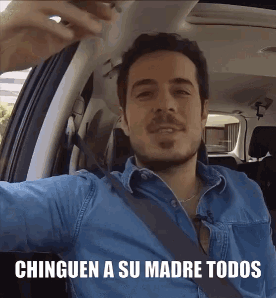 a man in a car with the words " chingen a su madre todos " on the screen