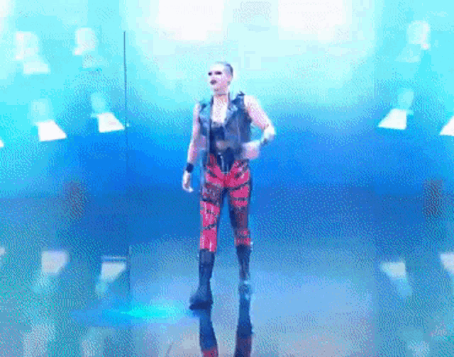 a man in a leather vest and red pants is dancing in front of a blue background