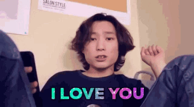 a man is holding a cell phone and wearing a shirt that says `` i love you '' .