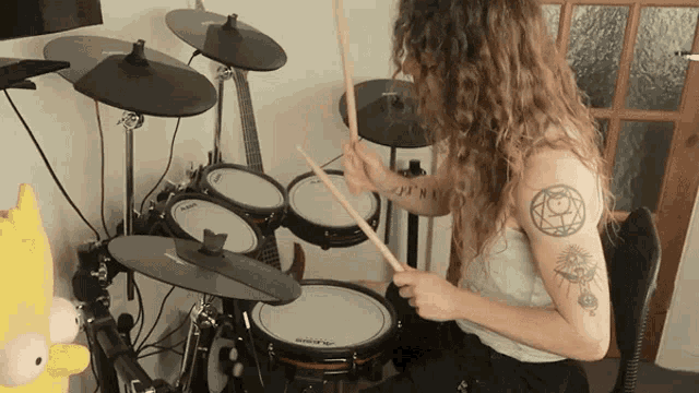 a woman with a tattoo on her arm playing a drum set