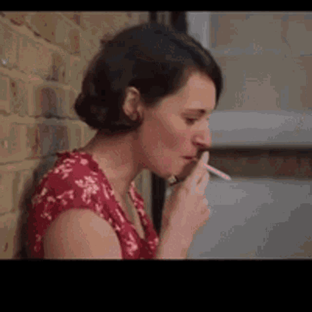 a woman in a red dress is smoking a cigarette against a brick wall .