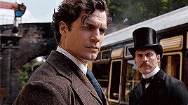 two men in suits and top hats are standing next to each other on a train platform .