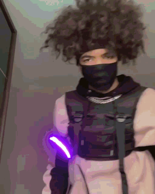 a man with curly hair is wearing a mask and holding a purple light .