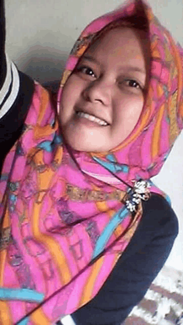 a woman wearing a pink and orange hijab is smiling .