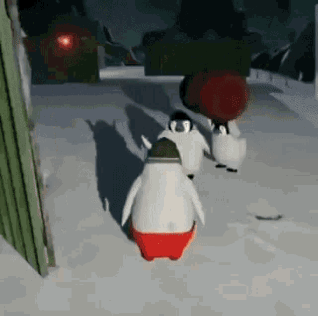 a group of penguins are walking in the snow . one of the penguins is wearing red underwear .