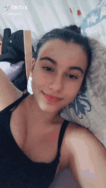a woman in a black tank top is laying on a bed and taking a selfie