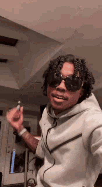 a man wearing sunglasses and a white hoodie is holding a lighter in his hand .