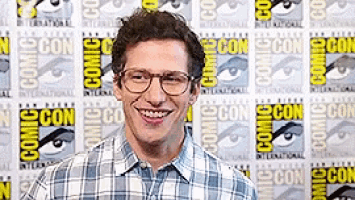 a man wearing glasses is smiling in front of a comic con poster