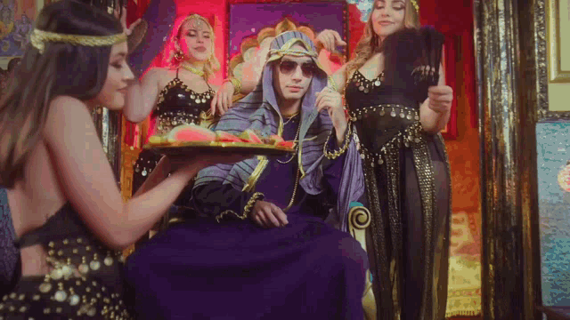 a man in a purple robe holds a tray of watermelon in front of two women