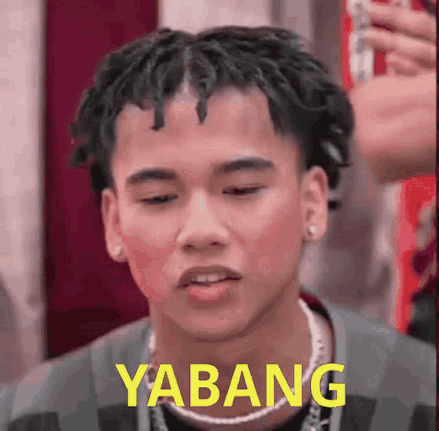 a young man with dreadlocks is wearing a necklace that says yabang on it