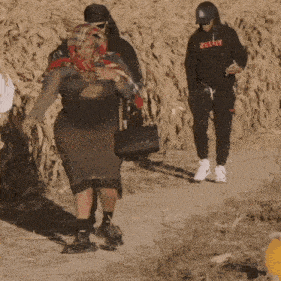 a woman wearing a scarf and a hoodie that says zelda walks down a dirt path