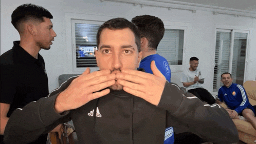 a man wearing an adidas sweatshirt is covering his mouth with his hands