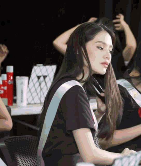 a woman in a black t-shirt with a white stripe on the shoulder is sitting in front of a mirror