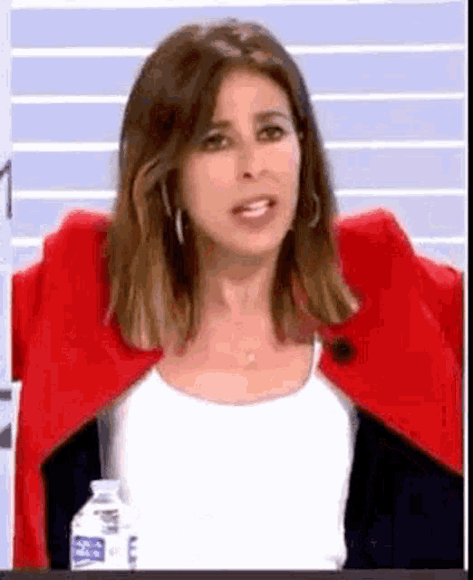 a woman wearing a red jacket and a white tank top is standing next to a bottle of water .