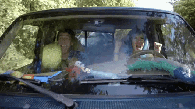 a woman with blue hair is driving a car with a man sitting in the back seat