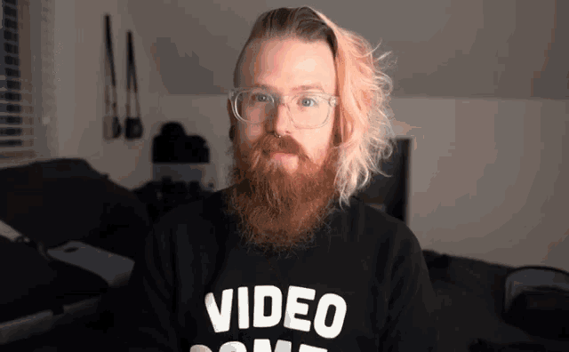 a man with glasses and a beard wears a black video game shirt