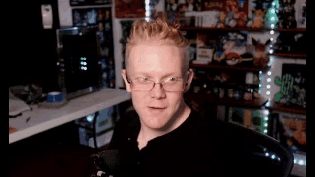 a man wearing glasses and a black shirt is sitting in front of a shelf with pokemon toys on it