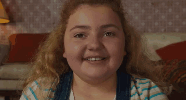 a young girl with long blonde hair is smiling for the camera while sitting on a couch .