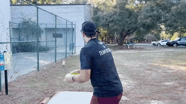 a man wearing a black shirt with the word team on it is throwing a frisbee in a park