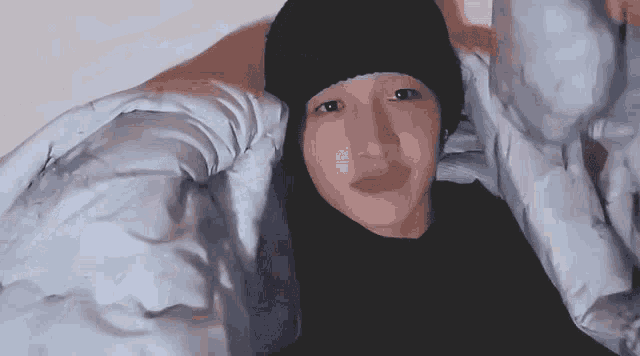 a person wearing a black hat is laying in bed with a blanket
