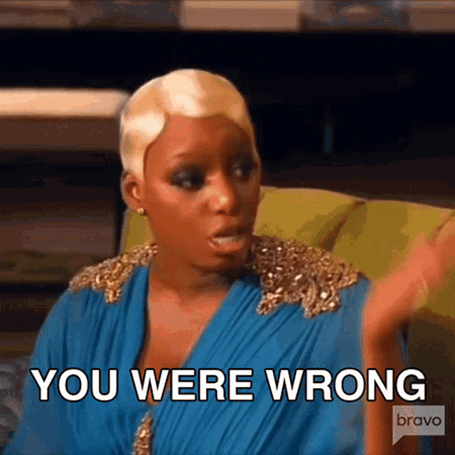a woman in a blue dress is sitting on a green couch and saying you were wrong .