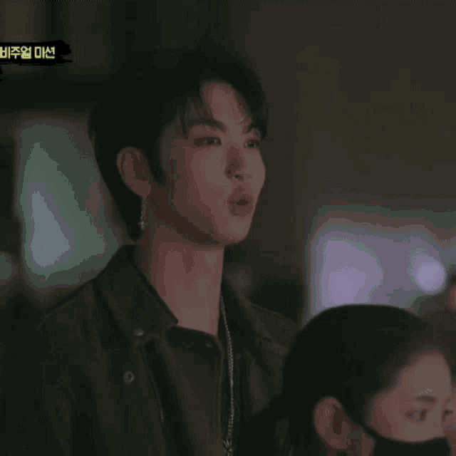 a man in a black leather jacket is standing in front of a sign that says ' 비주얼 미션 '