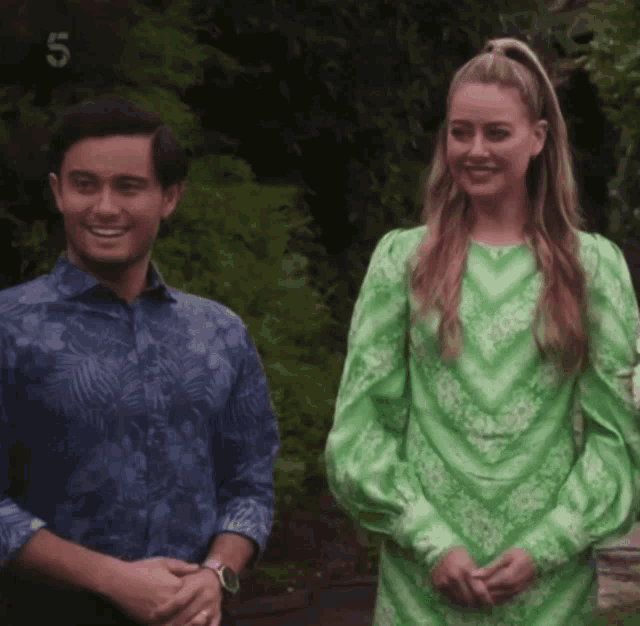 a man in a blue shirt and a woman in a green dress are standing next to each other and smiling