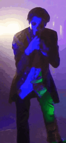 a man is standing in front of a microphone in a dark room with a blue light behind him .