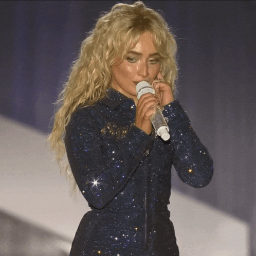 a woman singing into a microphone while wearing a sparkly blue dress