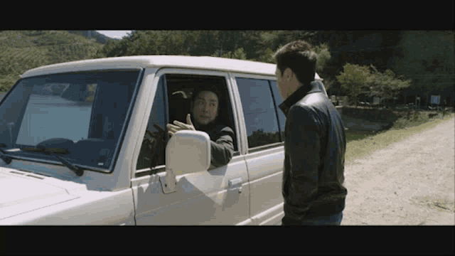 a man in a black leather jacket talks to another man in a white car