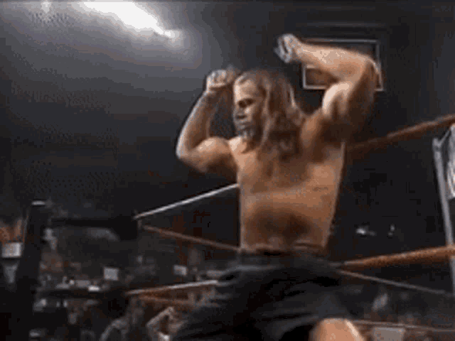 a shirtless wrestler flexes his muscles in a ring