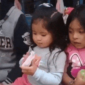 two little girls are sitting next to each other and one of them is holding a candy bar .
