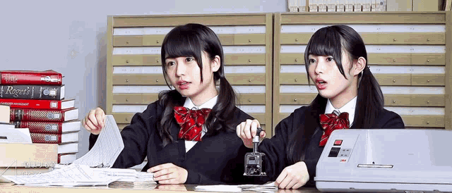 two girls are sitting at a desk with a stack of books including one titled recent