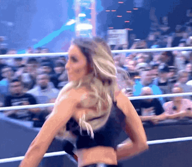 a woman in a black bra is standing in a ring with a crowd behind her