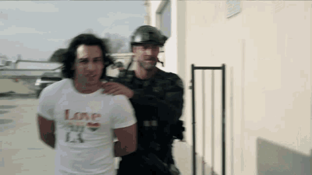 a man in a white shirt with the word love on it is being led by a police officer