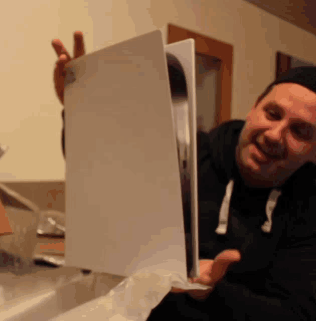 a man in a black hoodie is holding a ps5 console