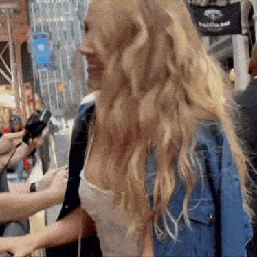 a woman in a denim jacket is being interviewed by a man in front of a sign that says buddie bar