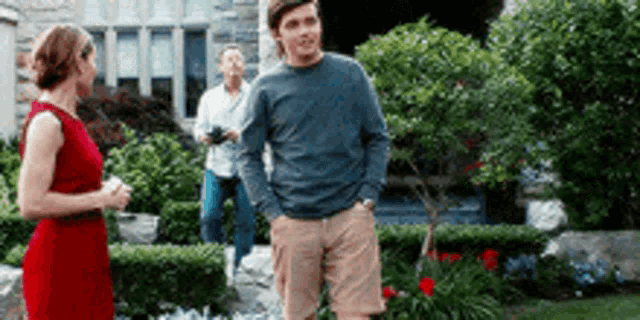 a man and a woman are standing in front of a house and talking to each other .