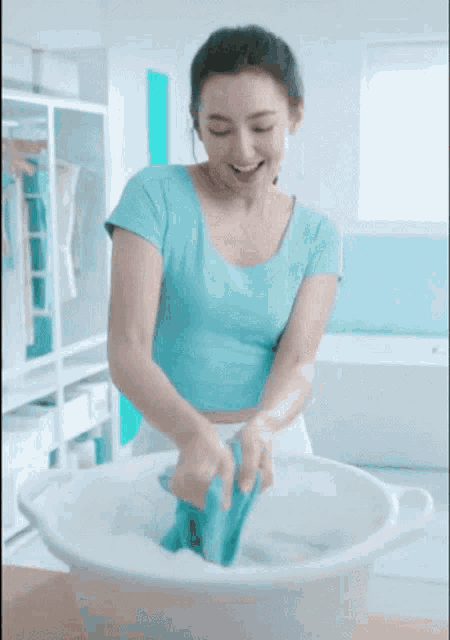 a woman in a blue shirt is washing clothes in a bucket
